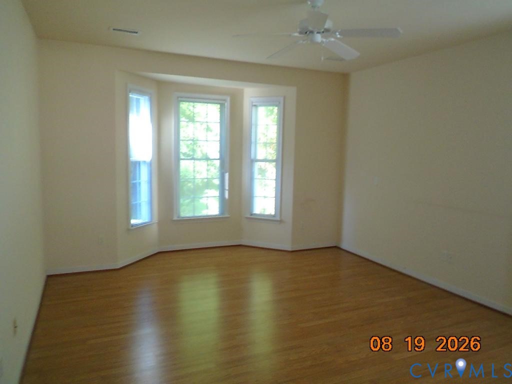 Bay window with three individual pane windows, wood-finish flooring, and a ceiling fan