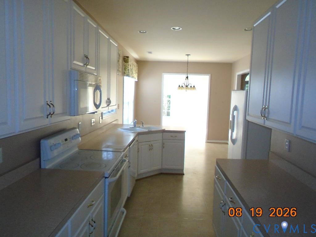 Expansive kitchen featuring white cabinetry, light-toned countertops, an integrated sink, an oven range, and a built-in microwave