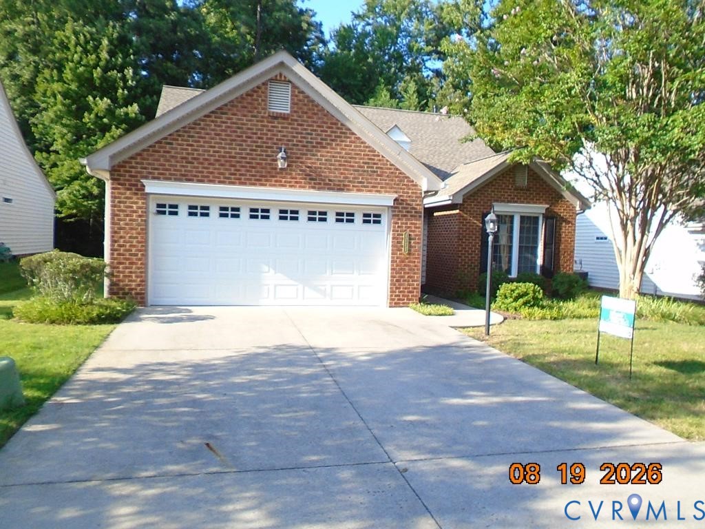 Brick exterior with a prominent two-car garage, concrete driveway, and mature landscaping