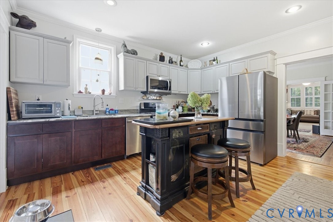 Kitchen featuring wood-finish flooring, two-tone cabinetry, stainless steel appliances, a center island with seating, and recessed lighting