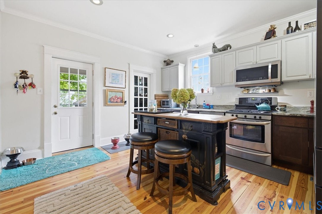 Kitchen featuring wood-finish flooring, recessed lighting, and a dark-toned island with seating granite counters