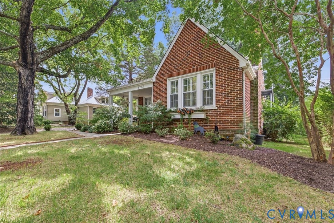 Brick exterior featuring white-frame windows, a covered front porch, and a landscaped yard with mature trees Brick exterior featuring white-frame windows, a covered front porch, and a landscaped yard with mature trees