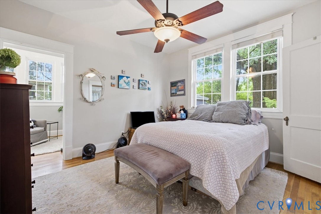 Main floor bedroom with hardwood flooring, painted interior walls, ceiling fan with light fixture, white trim detailing, and transom window