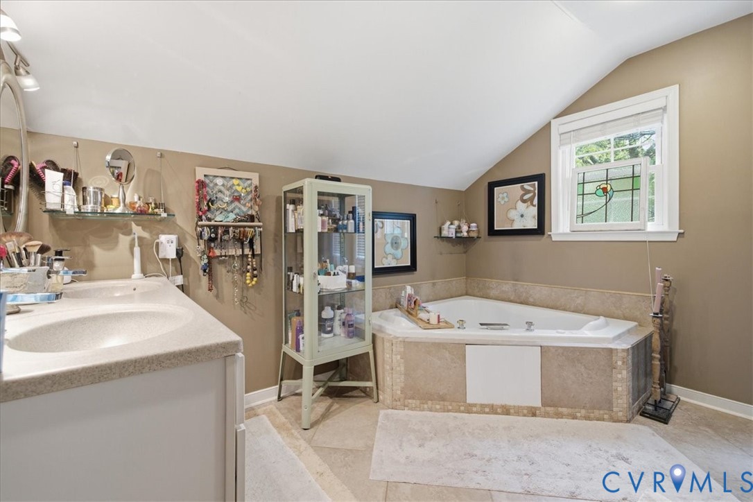 Angled soaking tub with tile surround, a built-in vanity with single basin, and a window with stained glass detail