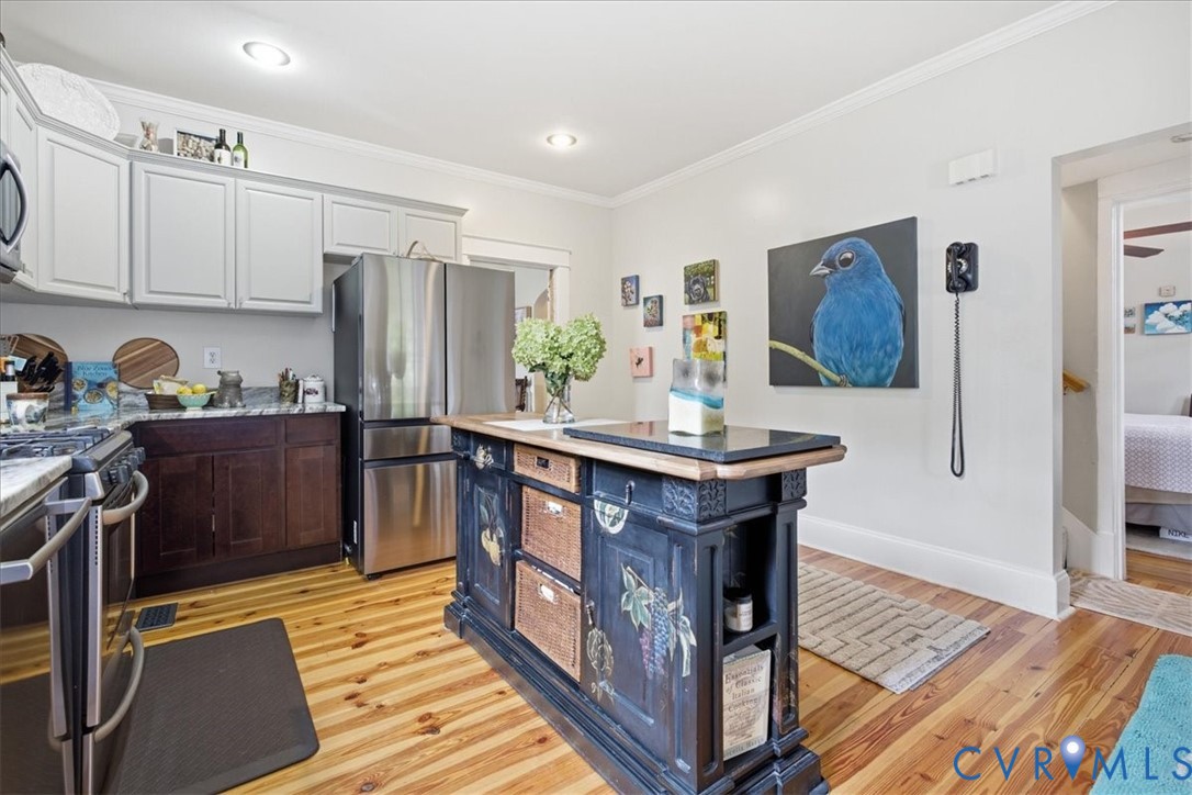 Kitchen featuring wood-finish flooring, two-tone cabinetry, stainless steel appliances, granite countertops, and a decorative island with a contrasting stone top