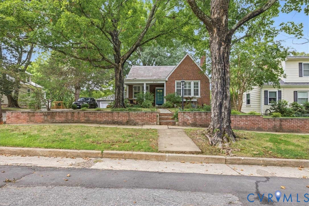 Brick exterior with white window trim, a covered front porch, and mature trees in the front yard Brick exterior with white window trim, a covered front porch, and mature trees in the front yard