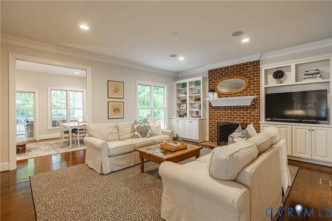 Built-in cabinetry, exposed brick fireplace, recessed lighting, crown molding, and hardwood flooring