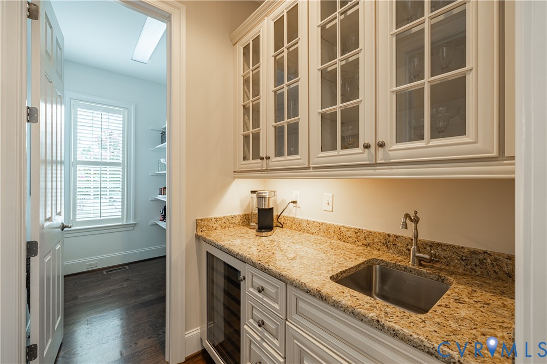 Built-in cabinetry with glass-front uppers, stone countertops, integrated sink with faucet, and a wine cooler