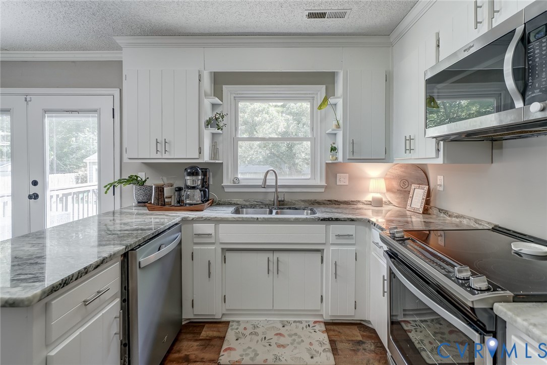 White cabinetry, stainless steel appliances, stone countertops, wood-finish flooring, and a double-door exterior access