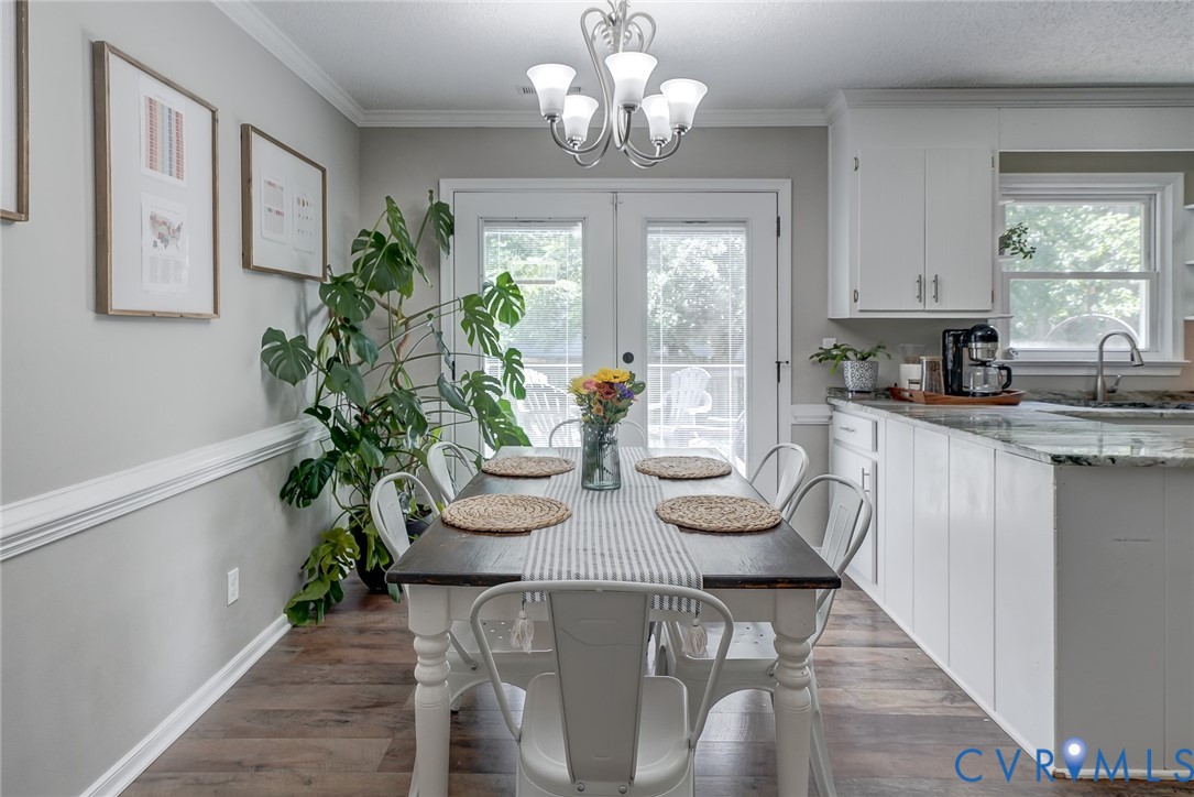Wood-finish flooring, white cabinetry, integrated sink, granite countertops, and a white framed glass-panel door
