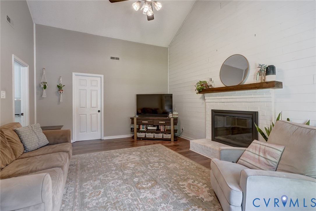 Vaulted ceiling, wood-finish flooring, white shiplap accent wall, fireplace with brick surround, and a wood mantel