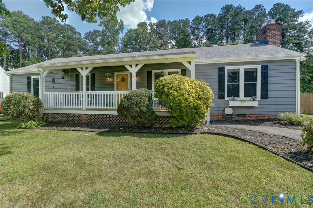 Gray siding exterior with white trim, covered front porch, white porch railing, and a brick chimney