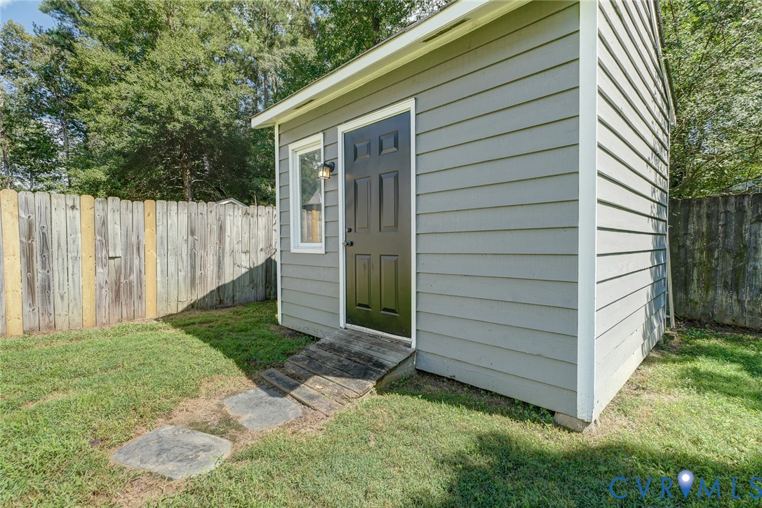 Detached auxiliary structure with horizontal siding, a paneled door, exterior lighting, a single window, and a wood ramp entry