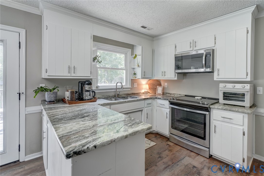 U-shaped kitchen with white cabinetry, stainless steel appliances, variegated stone countertops, and wood-finish flooring