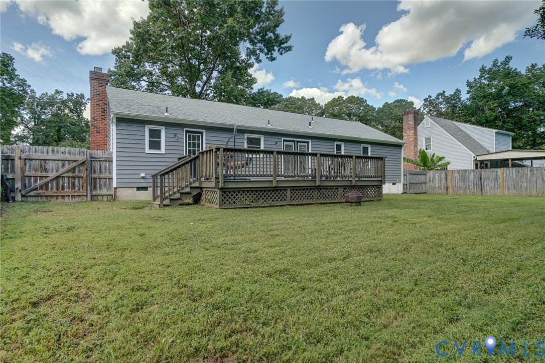 Expansive backyard featuring a large wooden deck with railings, grey horizontal siding, and two brick chimneys