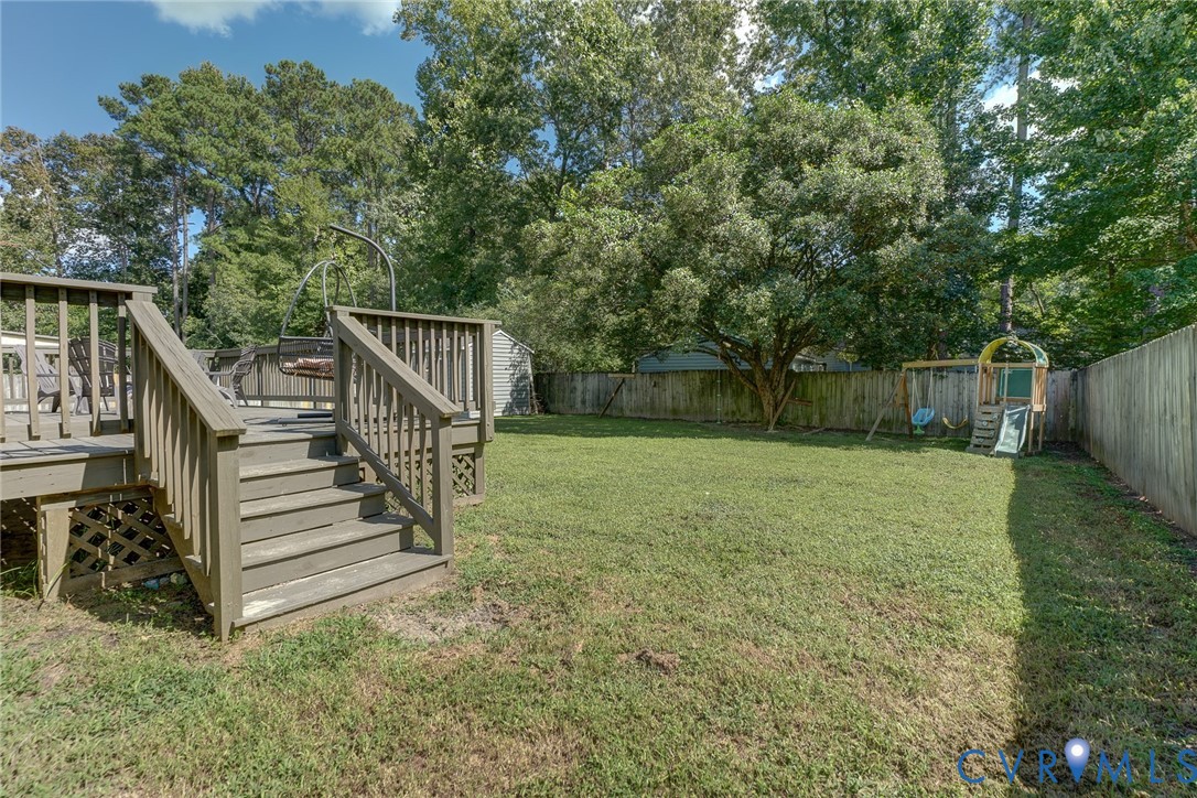 Expansive backyard featuring a wood deck with stairs, a privacy fence, and mature trees