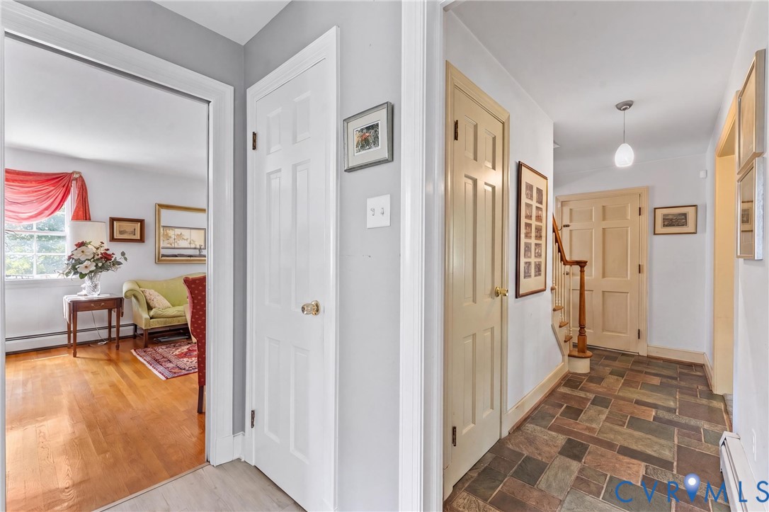 Hallway featuring multi-toned slate flooring, pendant light fixture, and wood staircase with banister