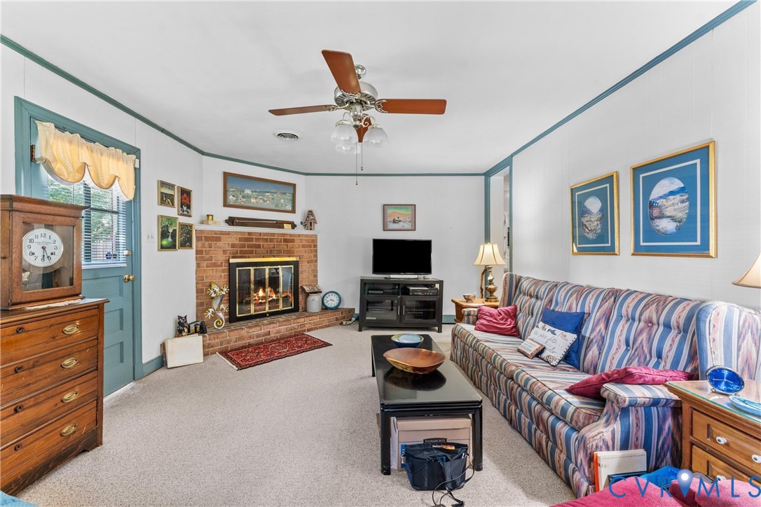Brick fireplace with a black metal screen, a ceiling fan with integrated lighting, and neutral carpeting