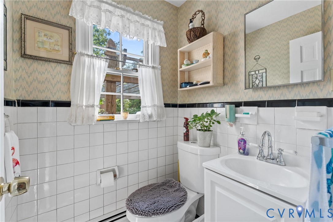 White tiled walls with a black accent border, pedestal sink with chrome faucet, and a wall-mounted mirror