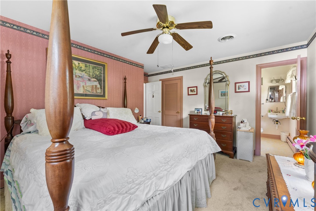 Carpeted flooring, ceiling fan with light fixture, and direct access to an attached bathroom featuring a pedestal sink and wall-mounted mirror