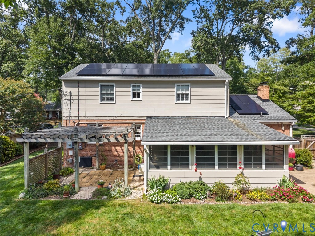 Rear exterior with multiple solar panels, a screened porch, and a pergola-covered patio with brick paving