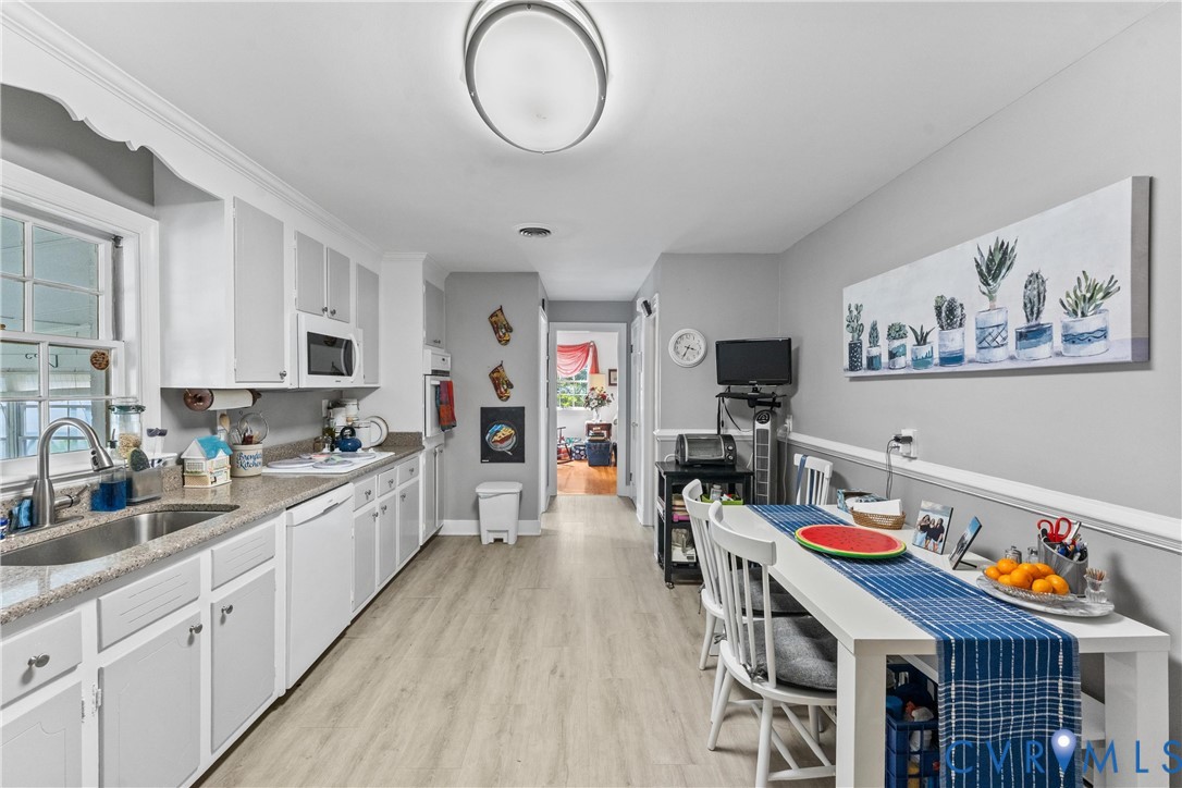 Galley kitchen featuring light wood-finish flooring, white cabinetry, a double basin sink, and a built-in microwave