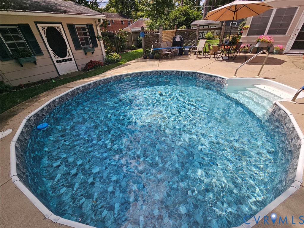 Oval-shaped pool with integrated steps, concrete surround, and adjacent shed with shuttered windows Oval-shaped pool with integrated steps, concrete surround, and adjacent shed with shuttered windows
