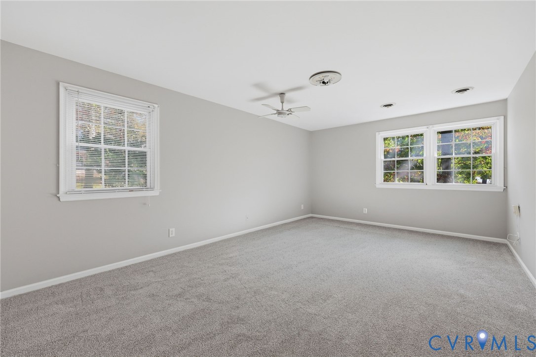 Neutral-toned interior space featuring wall-to-wall carpeting, dual multi-pane windows, and a ceiling-mounted fan