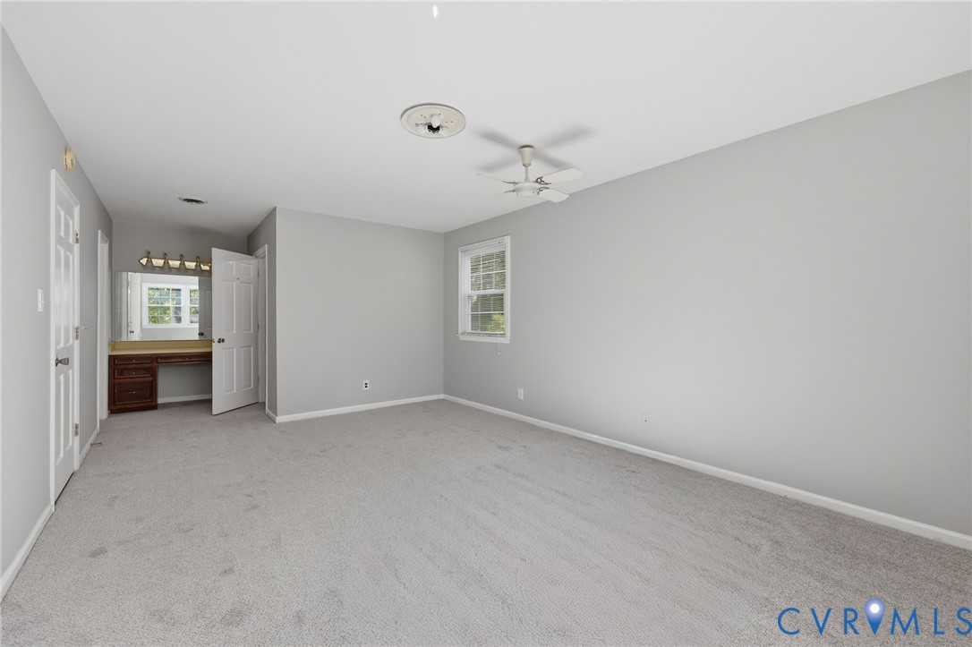 Neutral-toned carpeted flooring, built-in vanity with wood-finish cabinetry, multi-blade ceiling fan, and window with white trim
