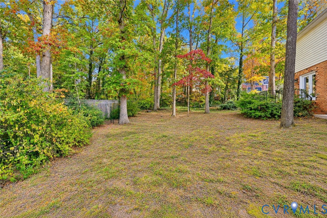 Expansive backyard featuring a brick exterior facade, mature trees, and natural landscaping