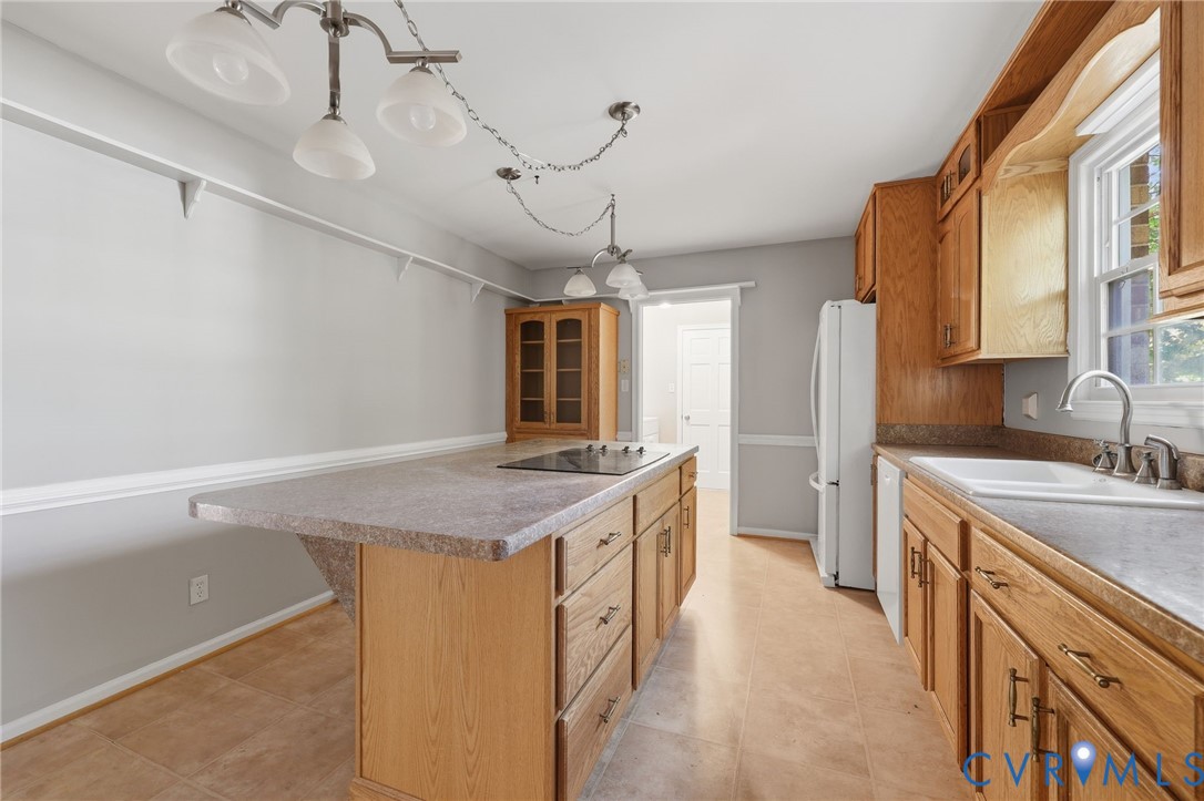 Kitchen featuring wood cabinetry, integrated island with a cooktop, double-basin sink, and multi-pendant lighting
