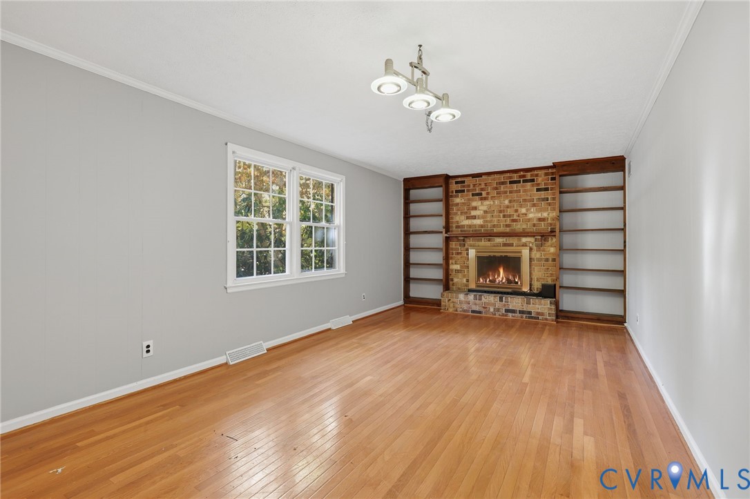 Living area featuring wood-finish flooring, brick fireplace with matching hearth, built-in shelving, and multi-pane window
