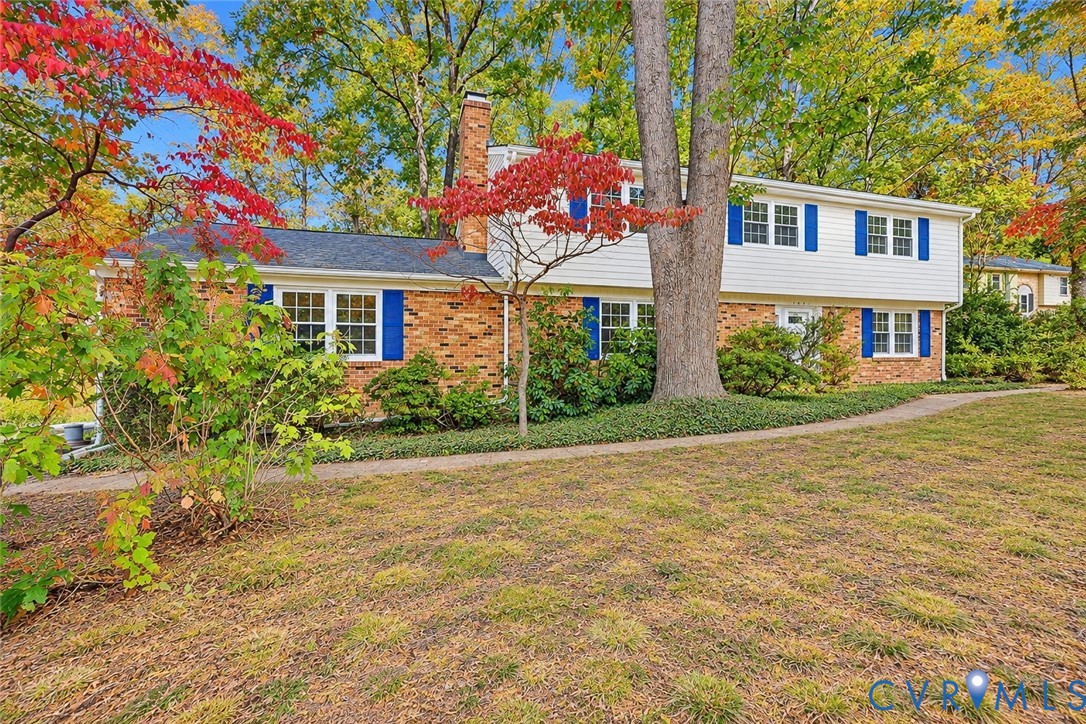 Two-story residence featuring a brick and horizontal siding exterior, blue window shutters, shingled roof, and a central brick chimney Two-story residence featuring a brick and horizontal siding exterior, blue window shutters, shingled roof, and a central brick chimney