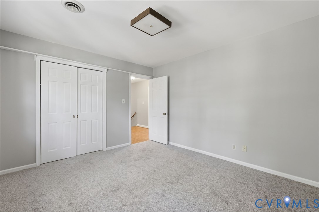 Neutral-toned interior space featuring carpeting, a square flush-mount light fixture, and a white double-door closet with a secondary swinging door