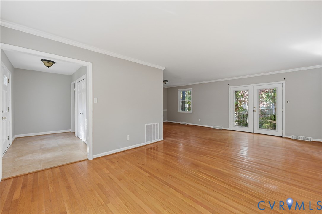 Hardwood flooring, neutral wall paint, crown molding, tile entryway flooring, and glass-paned double doors