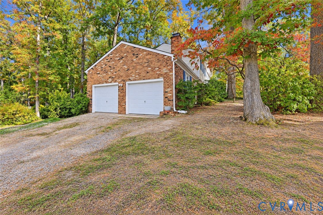 Multi-level brick exterior with an attached two-car garage and mature wooded surroundings