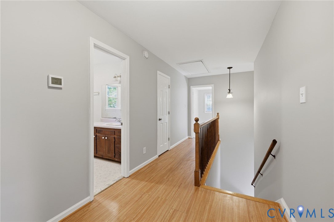 Hallway featuring wood-finish flooring, a wooden staircase railing with a matching handrail, and a pendant light fixture