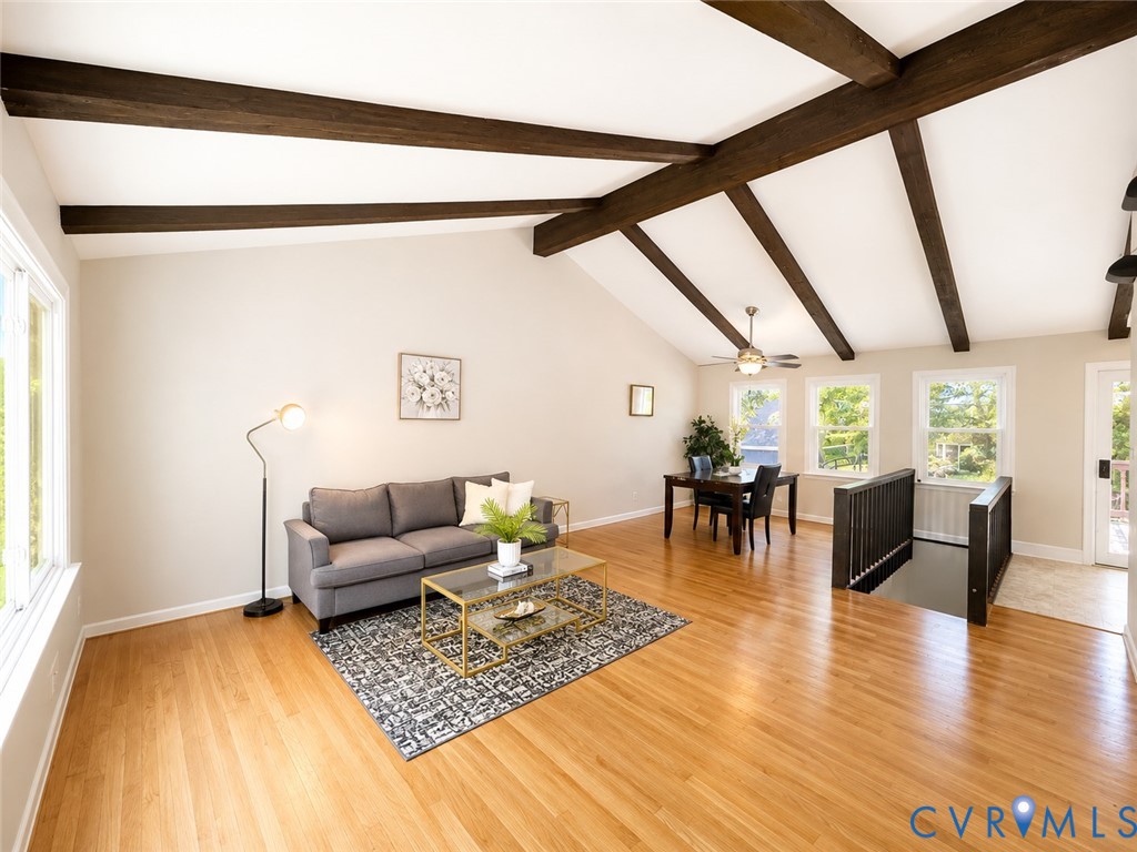 Vaulted ceiling with exposed wood beams, wood-finish flooring, multiple windows, and a ceiling fan