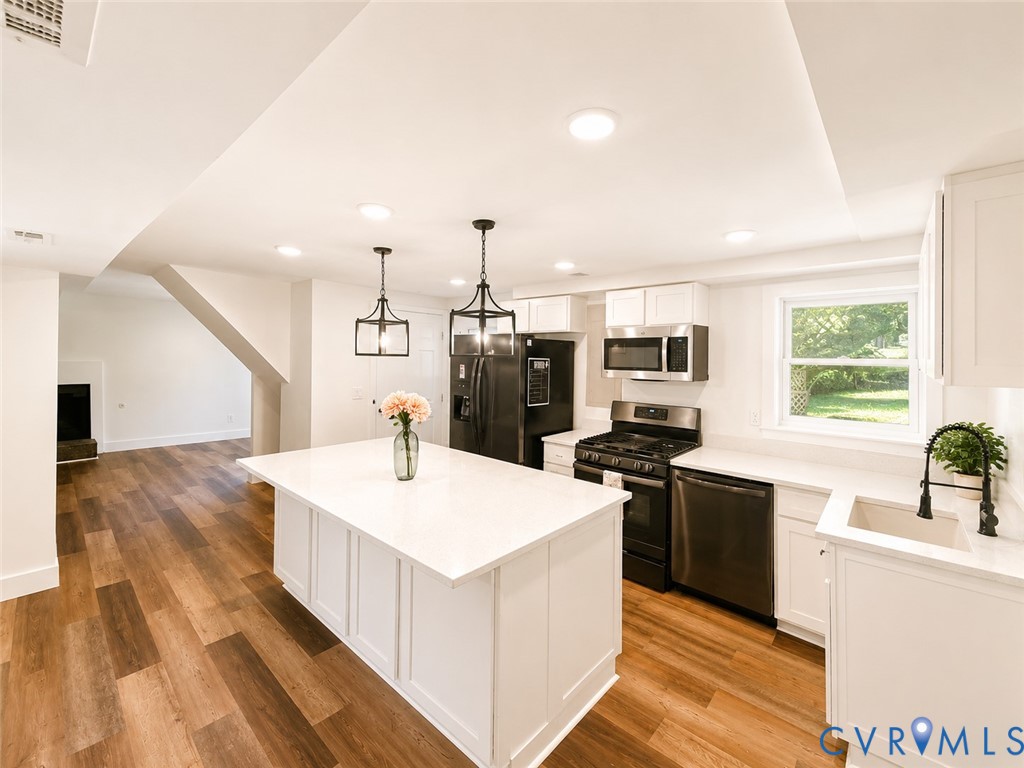 Open-concept kitchen with a central island, recessed lighting, wood-finish flooring, white cabinetry, and stainless steel appliances