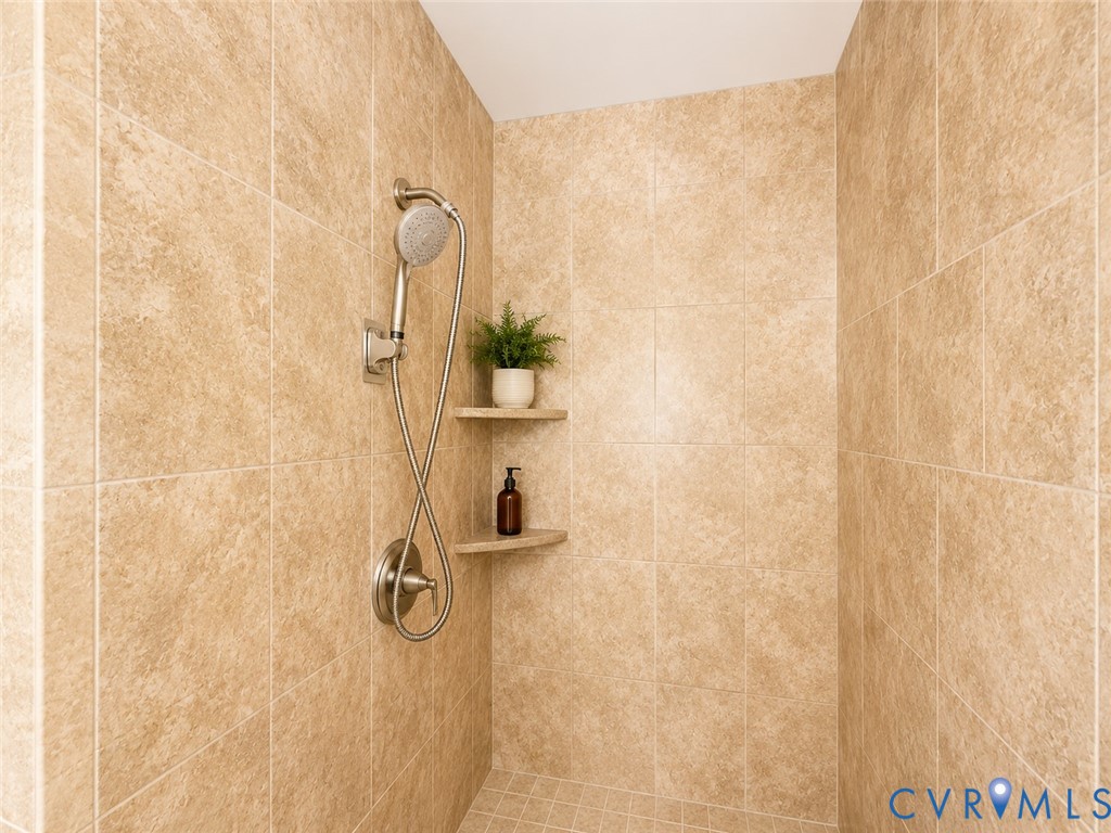 Tiled shower enclosure featuring a handheld showerhead, brushed nickel fixtures, and built-in corner shelving