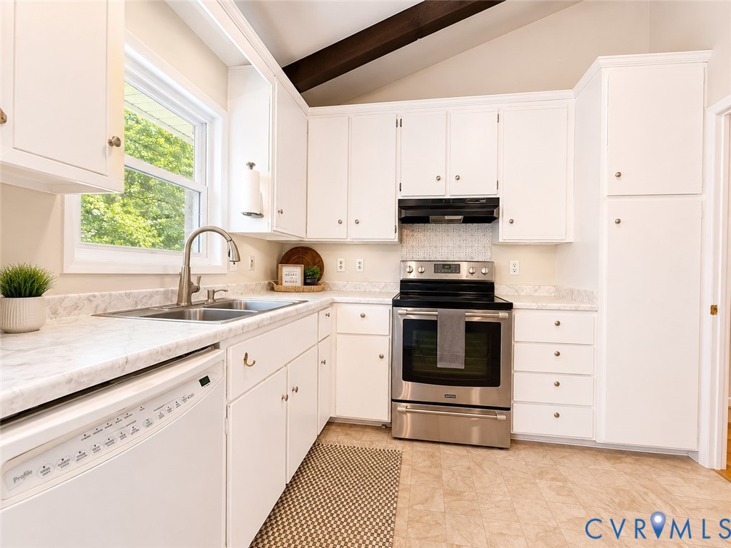Kitchen featuring white cabinetry, a stainless steel range with overhead ventilation, a dual basin stainless steel sink with a gooseneck faucet, light-toned countertops, and exposed ceiling beams
