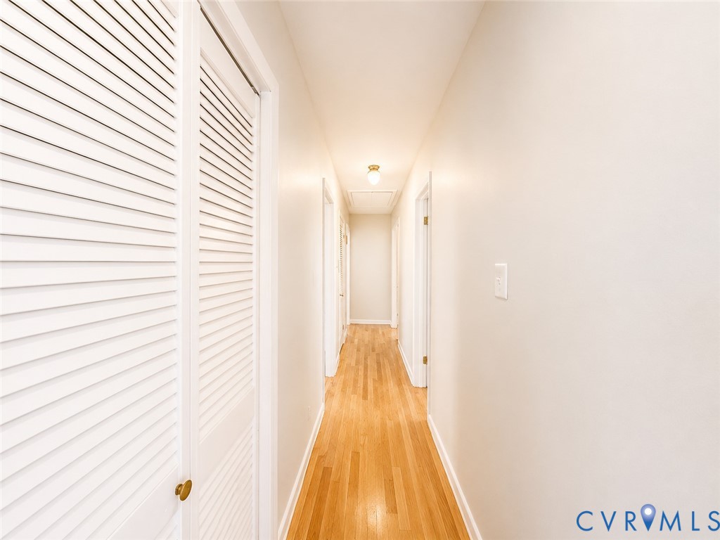 Hardwood flooring extends throughout the hallway, featuring white louvered closet doors and a flush-mount ceiling light fixture