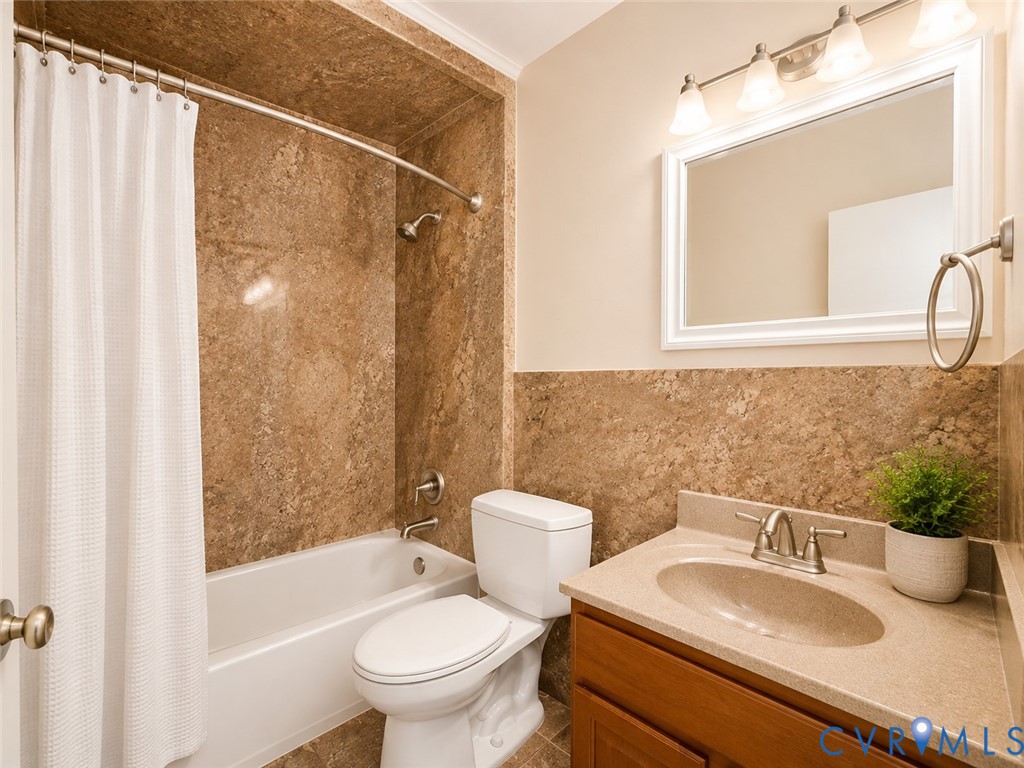 Bathroom featuring a built-in tub with a shower fixture, wall-mounted vanity light, framed mirror, and a wood-finish vanity with an integrated sink