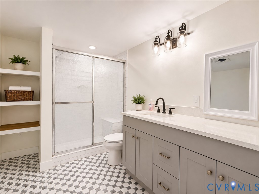 Spa-inspired primary bathroom featuring a frameless glass-enclosed shower with subway tile surround, dual-sink vanity with soft-close cabinetry and brushed nickel hardware, quartz countertop, black framed mirror, and geometric tile flooring