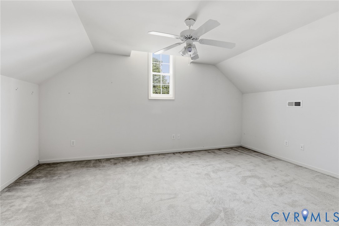 Attic room with sloped ceilings, a single window, and a white ceiling fan
