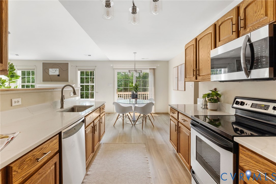 Open-concept kitchen featuring wood cabinetry, light countertops, and stainless steel appliances, with wood-finish flooring extending to the dining area with a glass sliding door