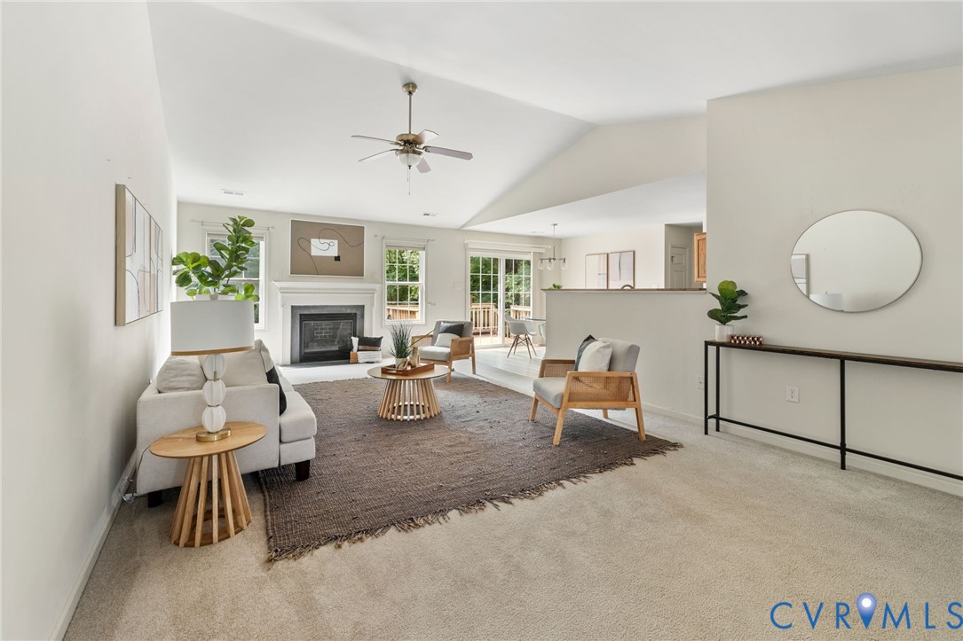 Carpeted living area featuring a vaulted ceiling with a ceiling fan, a fireplace with a white mantel, and a sliding glass door