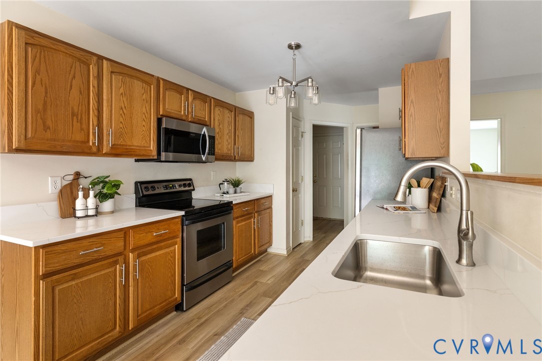 Kitchen featuring wood-finish cabinetry, stainless steel appliances, white countertops, a stainless steel sink, and wood-finish flooring