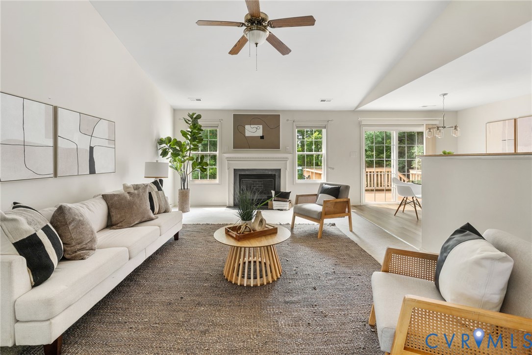 Vaulted ceiling with a ceiling fan, fireplace with a mantel, multiple windows, and sliding glass doors opening to an outdoor deck