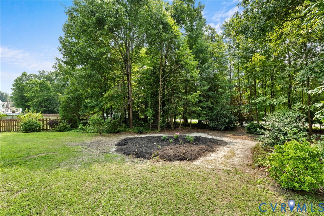Expansive lawn with a treed perimeter, featuring a garden bed and a wooden fence